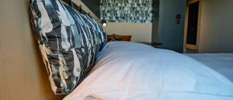 A bed with a patterned pillow and white sheets, a hanging light fixture, and a door in the background.