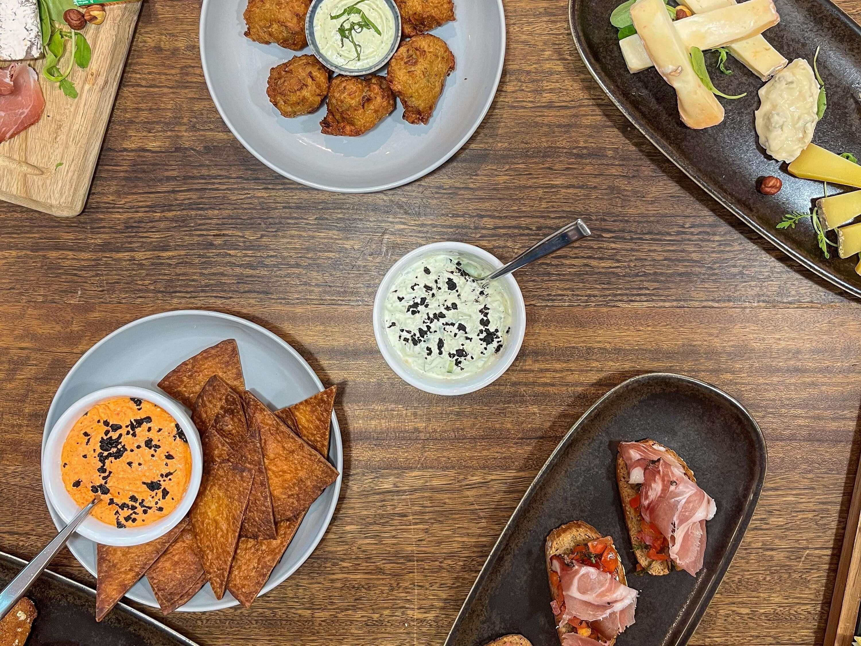 A variety of food items on a wooden table, including fried items, cheese, and dips.