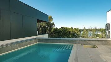 A modern outdoor pool area with a clear blue pool, surrounded by a low wall and a metal railing.