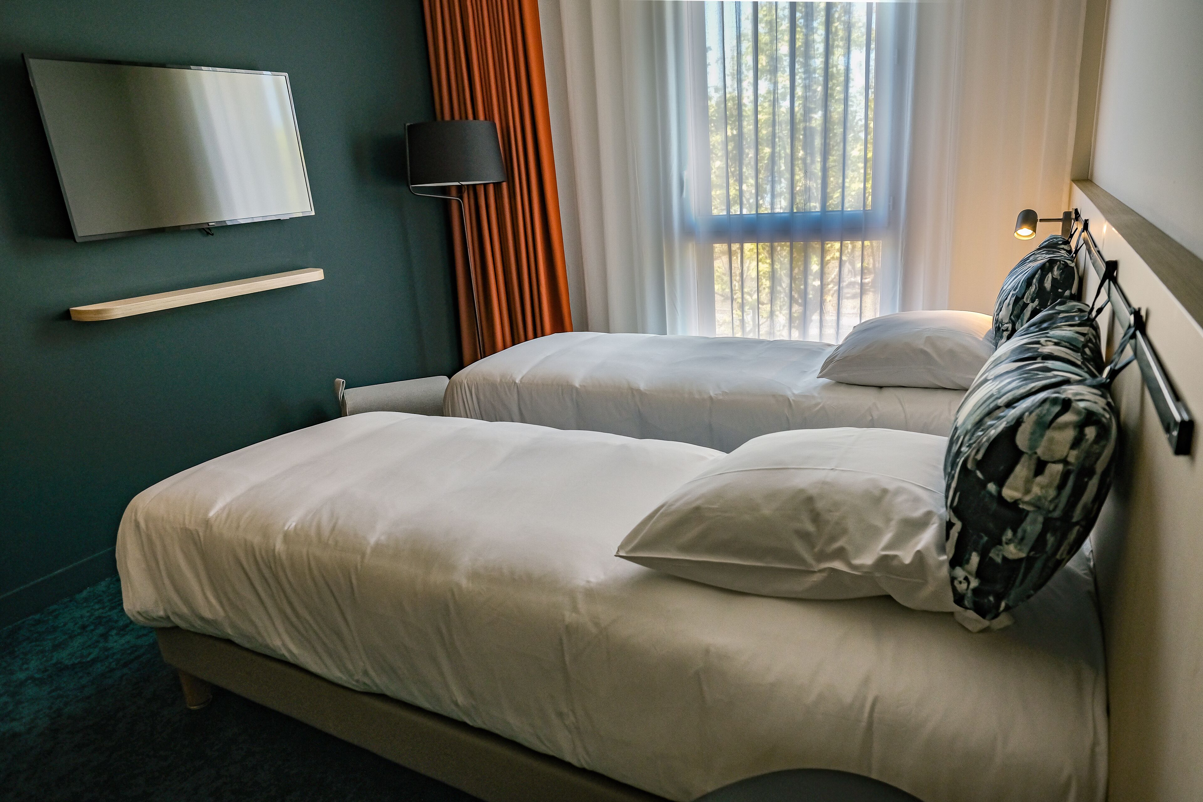 A hotel room with two beds, a TV, a bedside table, and a window with curtains.