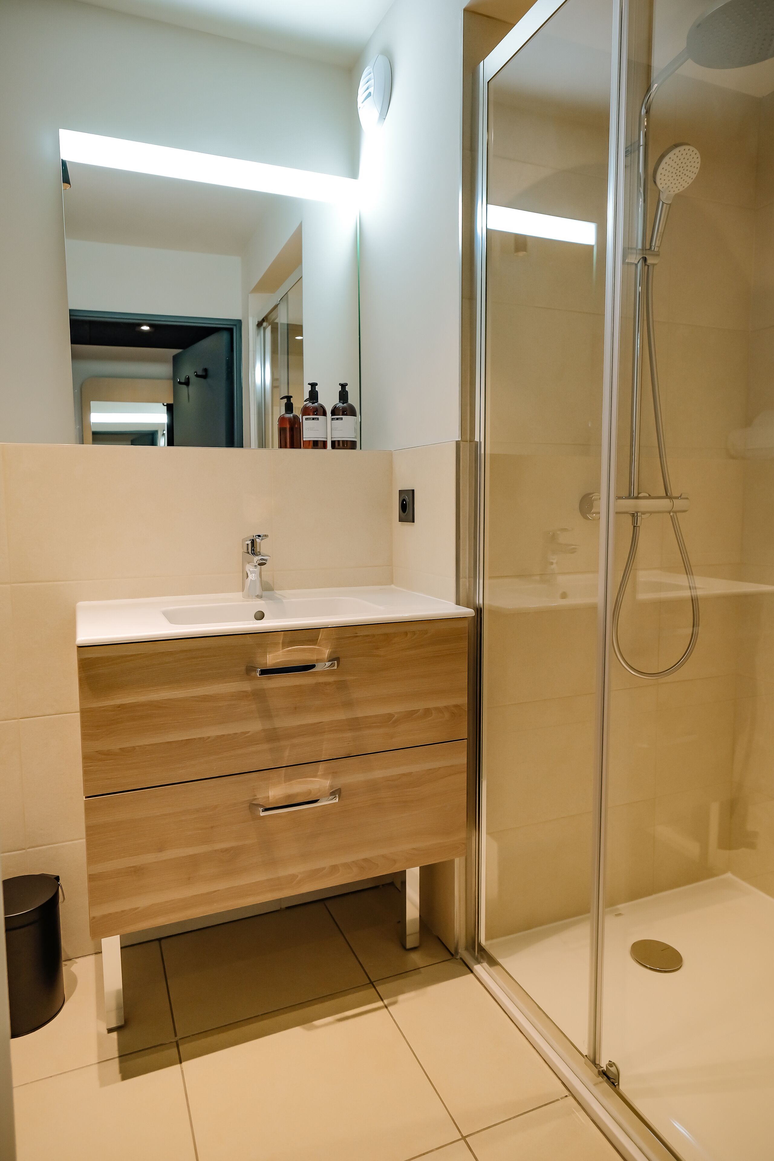 A modern bathroom with a glass-enclosed shower, a white sink, and wooden vanity drawers.