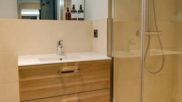 A modern bathroom with a glass-enclosed shower, a white sink, and wooden vanity drawers.