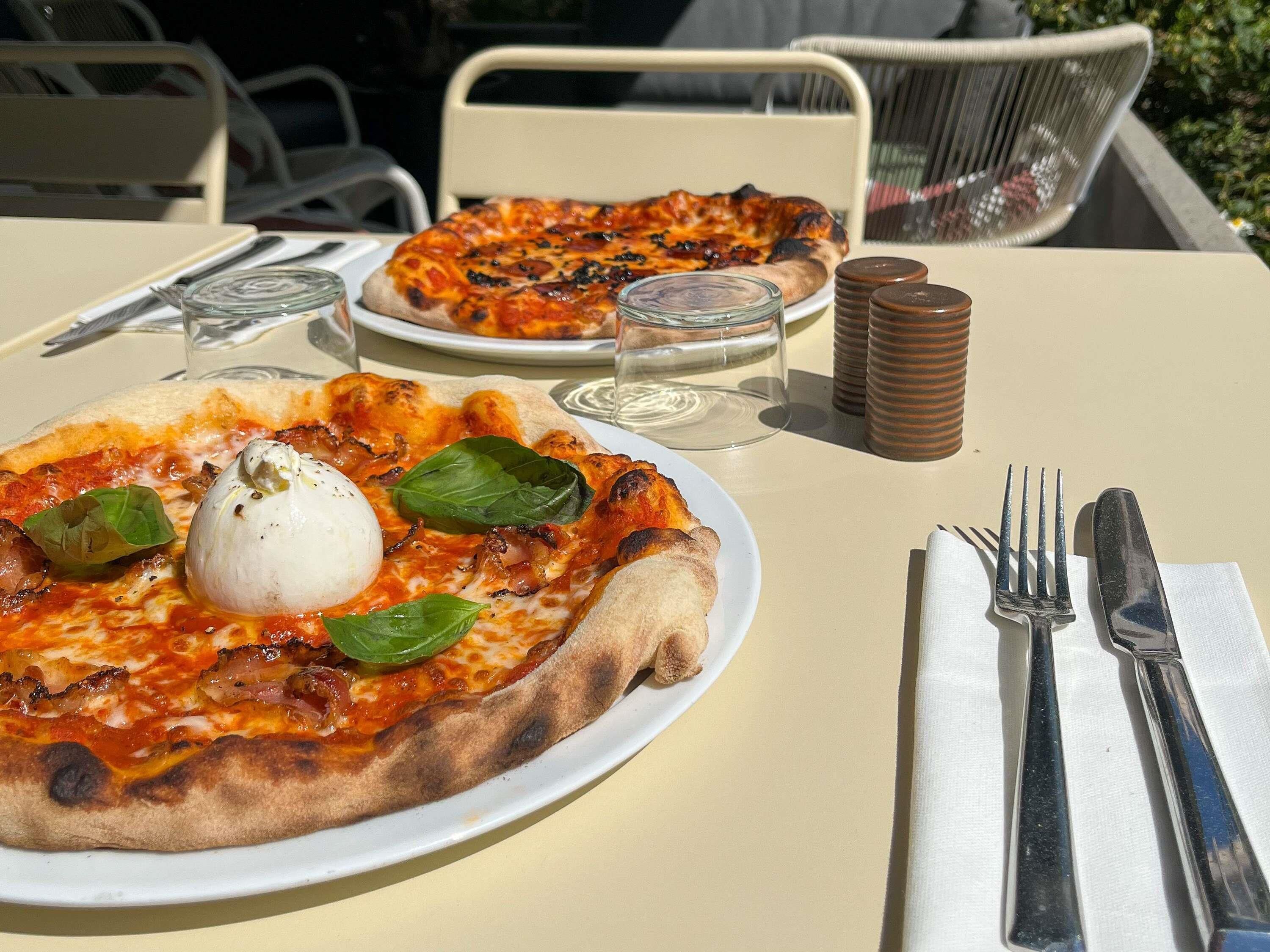 A table with a pizza, a glass, and a napkin with cutlery.