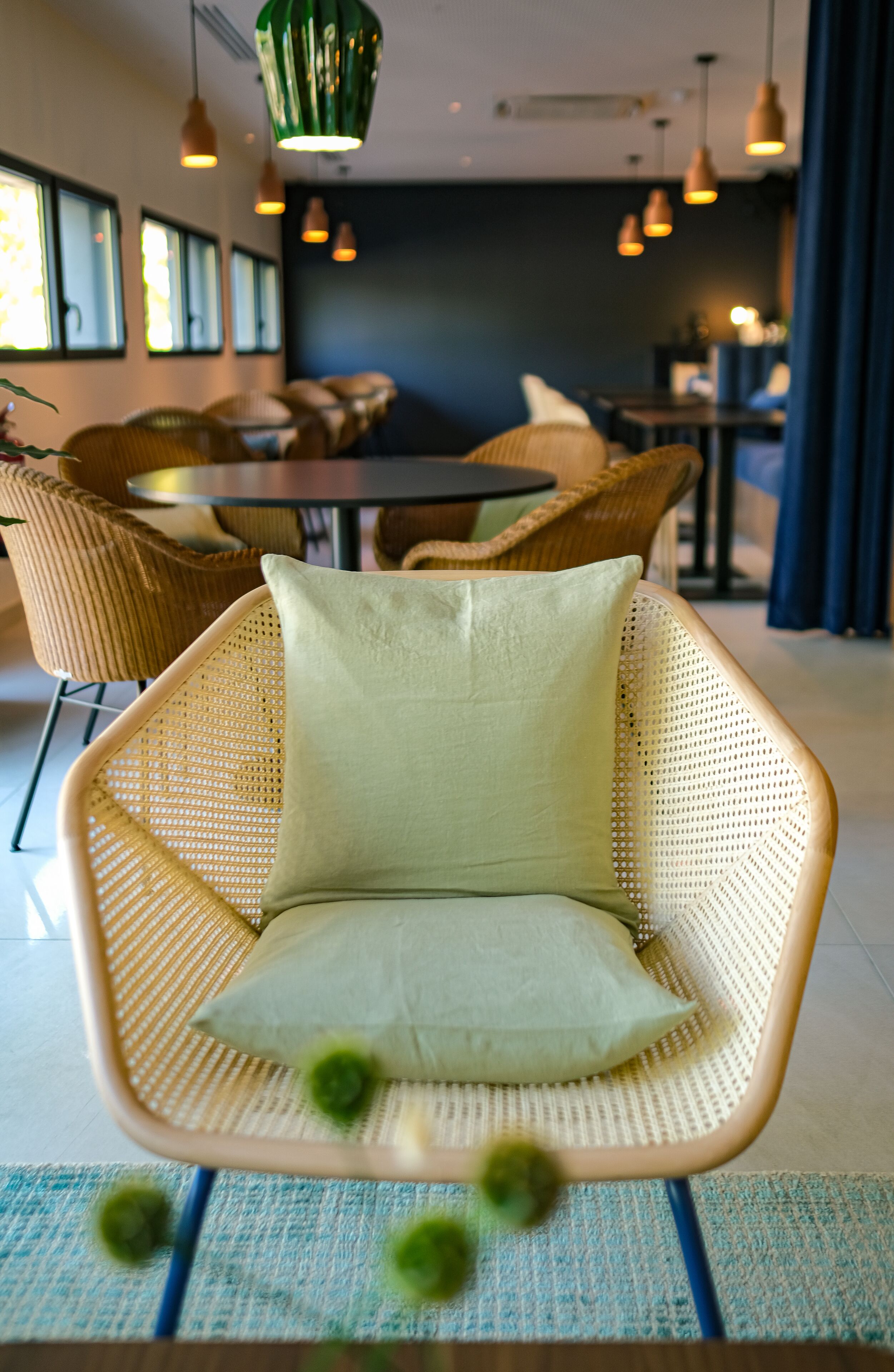 A wicker chair with a cushion in a modern interior space with hanging pendant lights and wicker furniture.