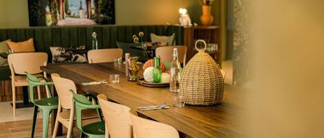 A dining area with a wooden table, green and beige chairs, hanging green pendant lights, and a woven basket on the table.