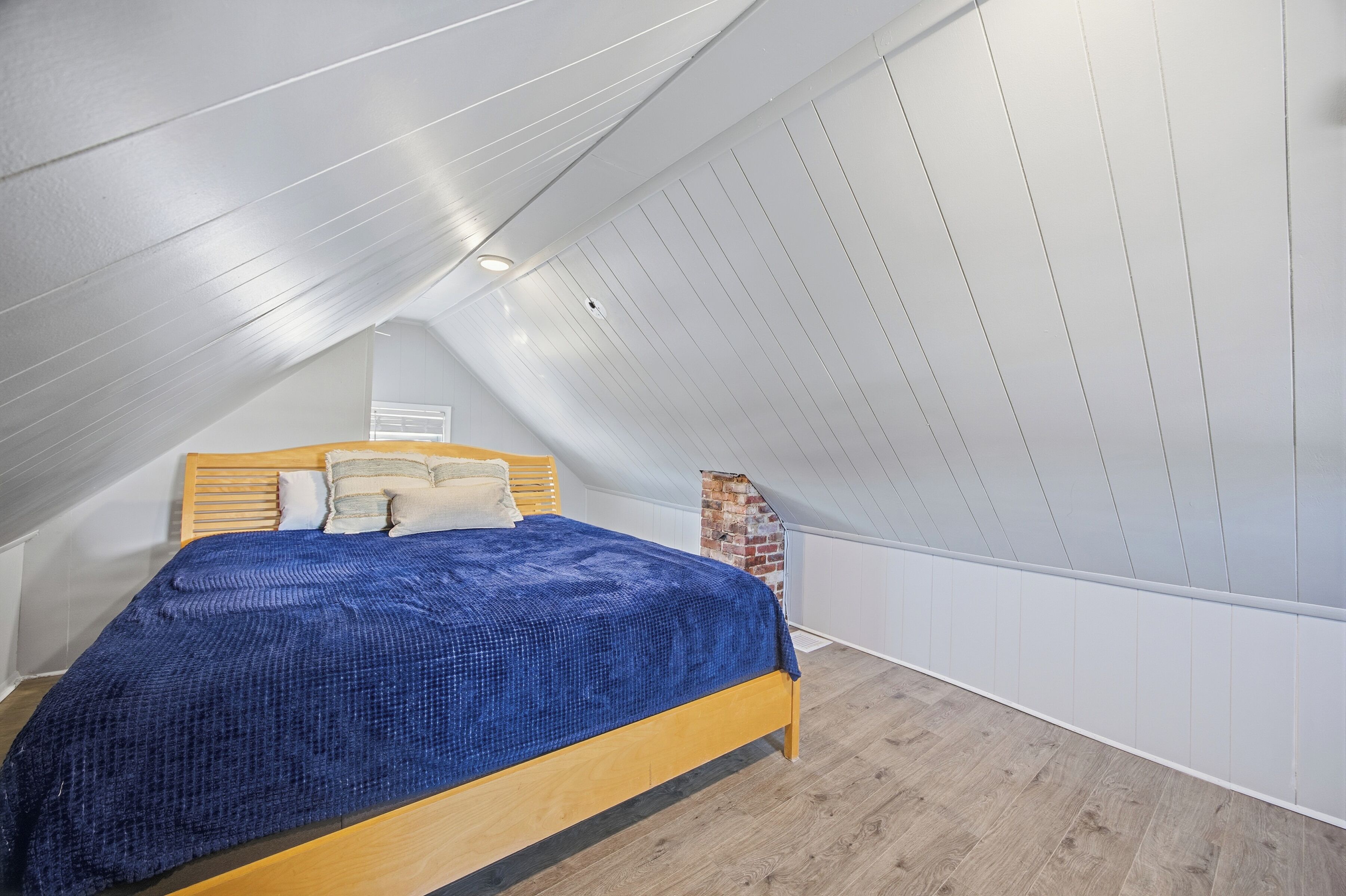 A bedroom with a sloped ceiling, a wooden bed, and a brick accent wall.