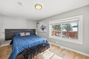 Een slaapkamer met een groot bed, een bankje, een raam met uitzicht op een terras en een plafondlamp.