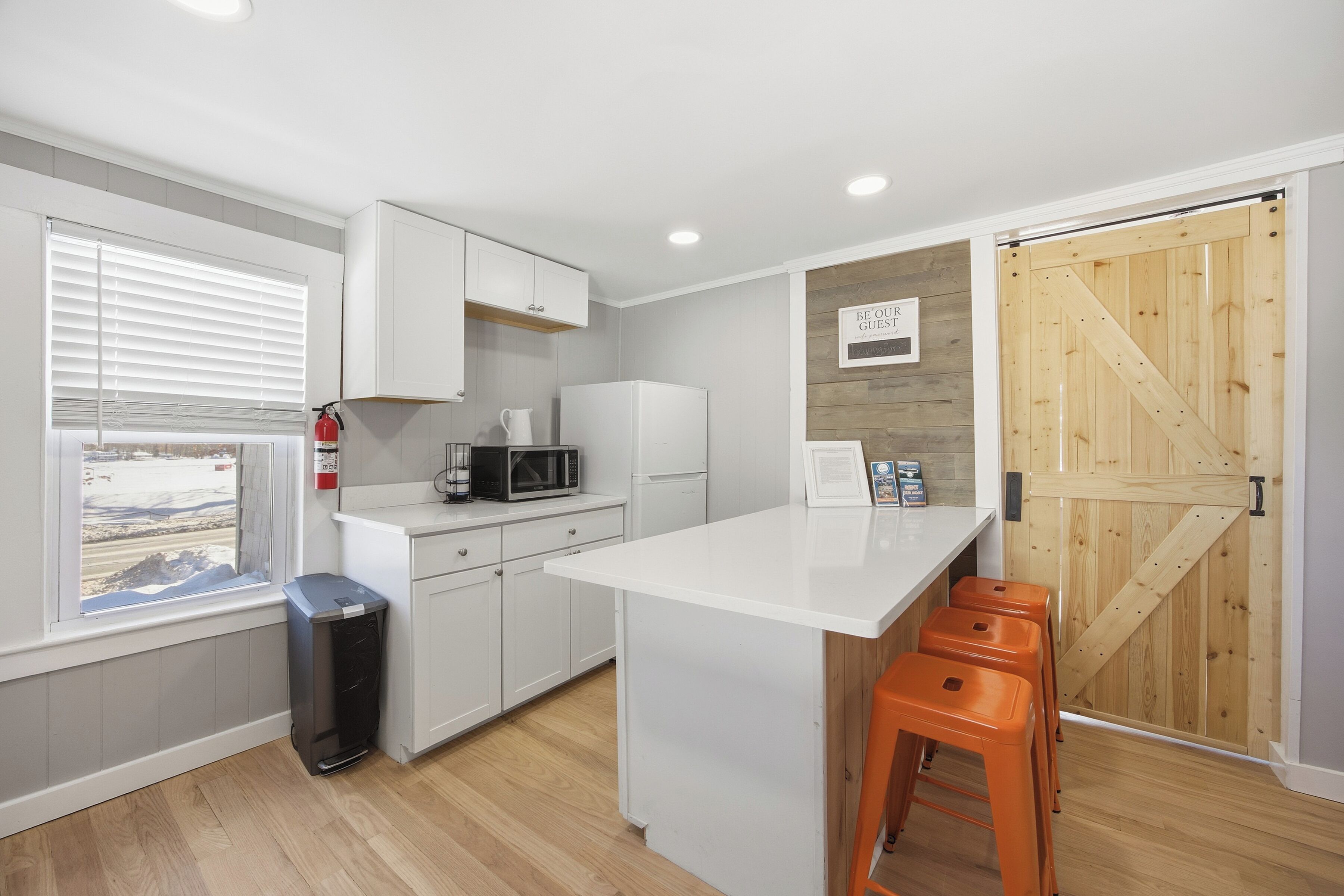 A modern kitchen with white cabinets, a microwave, and a wooden door.