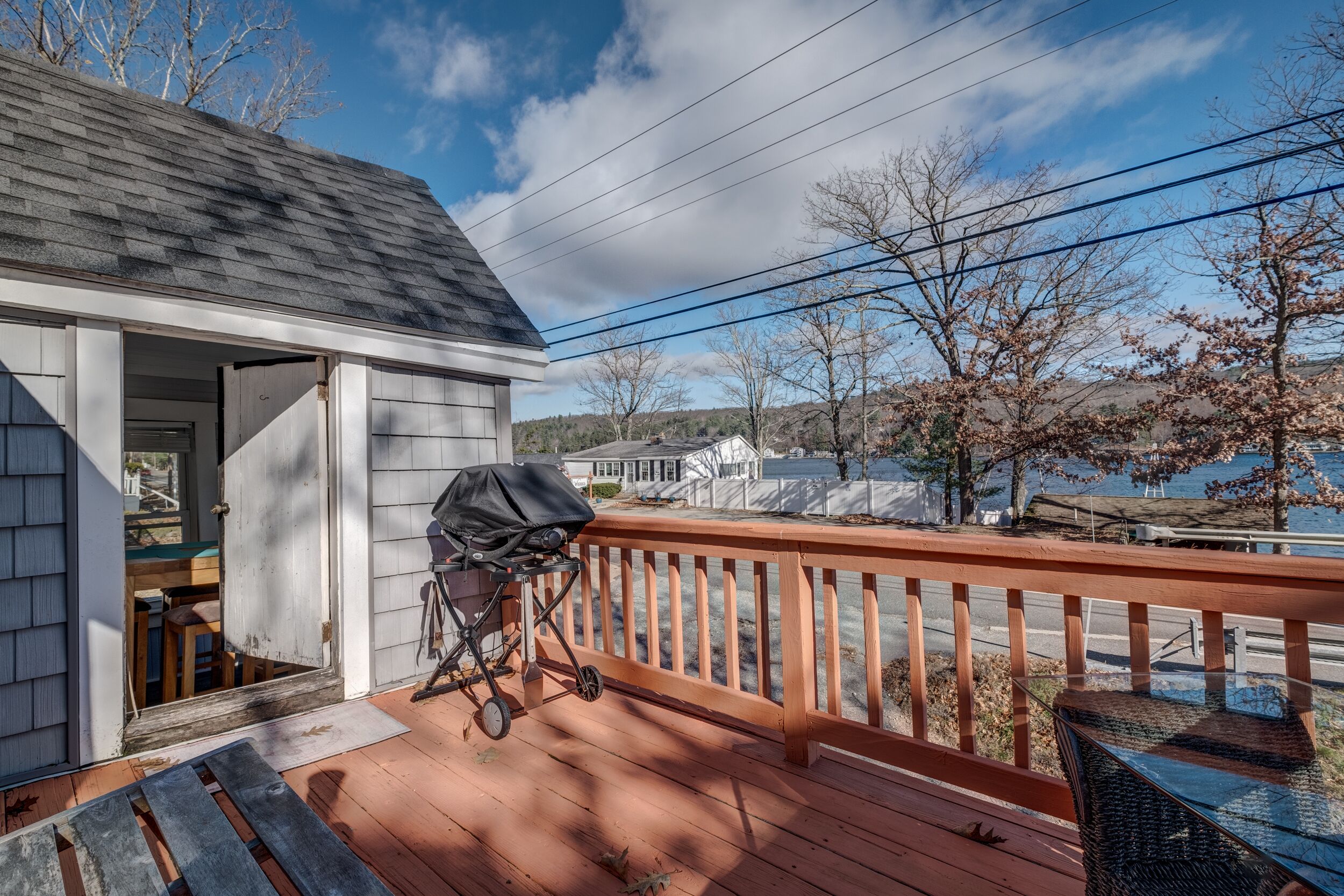 Une terrasse en bois avec une rambarde, un barbecue couvert et une vue sur un lac et des collines.