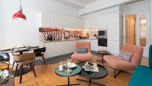 A modern living room with a dining area, a kitchen in the background, and a red pendant light.