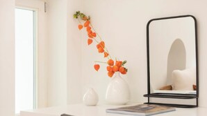A white desk with a mirror, a vase with orange flowers, and a book.