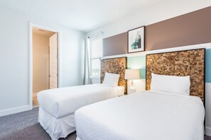 Ein Hotelzimmer mit zwei Betten, einem Holz-Kopfteil, einem Nachttisch mit Lampe und einem Fenster mit Jalousien.