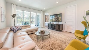 A modern living room with a sectional sofa, a glass coffee table, and a television on a stand. - Encore Reunion Home: Game Room & Waterpark Access - 371FL (Reunion)
