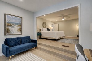Un dormitorio con una cama, un sofá azul, un cuadro y un ventilador de techo.