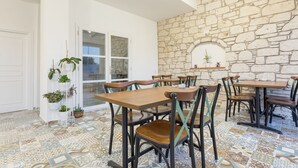 A dining area with stone walls, multiple tables and chairs, and potted plants. - Melekaki Alacati (Cesme)