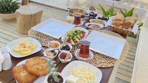 A poolside dining area with a table set for a meal, including various dishes and drinks, surrounded by lounge chairs and a pool. - Melekaki Alacati (Cesme)