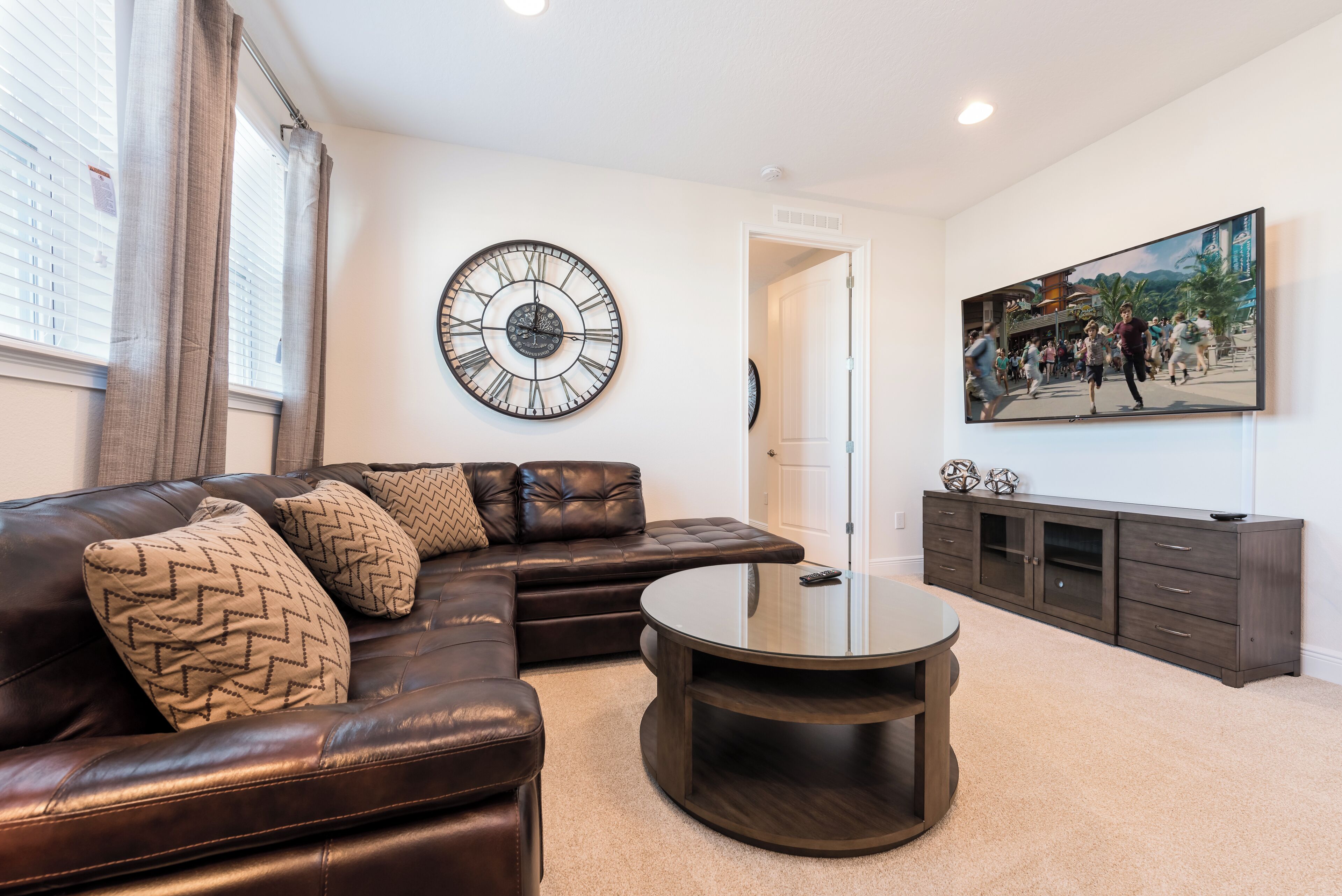 A living room with a leather sofa, a round coffee table, a wall clock, a cabinet, and a painting.