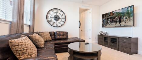 A living room with a leather sofa, a round coffee table, a wall clock, a cabinet, and a painting.