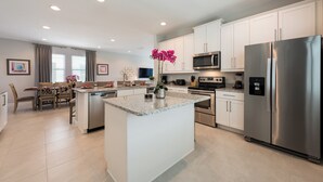 A modern kitchen with white cabinets, stainless steel appliances, and a granite island. - Delightful Home near Disney: Private Pool, Media Room & Waterpark - 7418MR (Reunion)