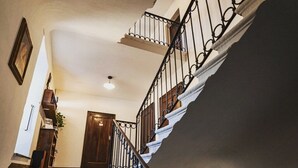 Una escala amb una porta de fusta al capdamunt, barana metàl·lica i una prestatgeria penjada a la paret amb llibres i una planta.