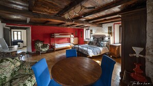 Habitació amb sostre de fusta, taula rodona de fusta, cadires blaves, un llit superposat i una paret vermella.