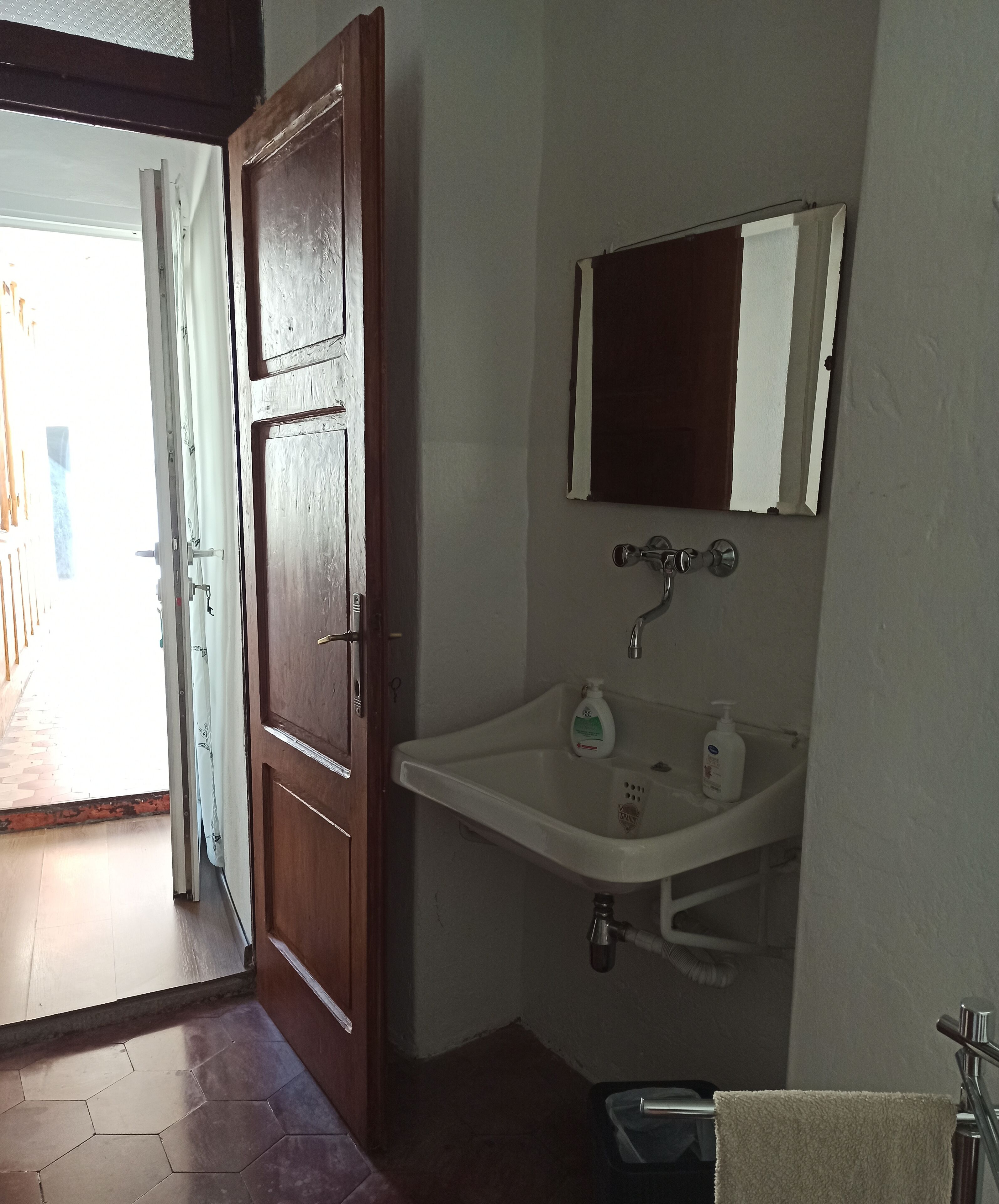A bathroom with a wooden door, a white sink, and a mirror above it.