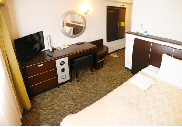 Habitación de hotel con cama, escritorio con televisor, espejo, armario y una pequeña zona de estar.