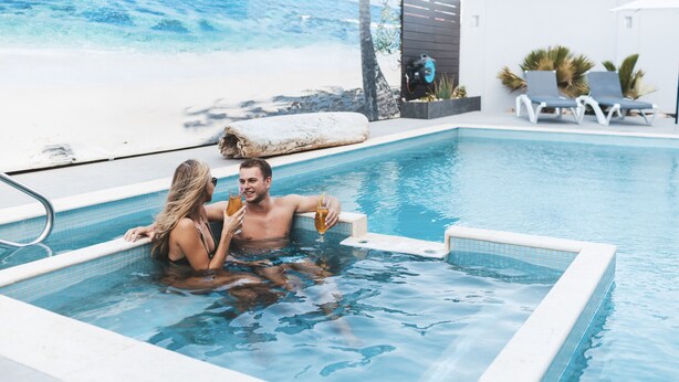 A swimming pool with a view of the beach, lounge chairs, and a water filtration system. - Gray Door Apartments - Adults Only (Noord)