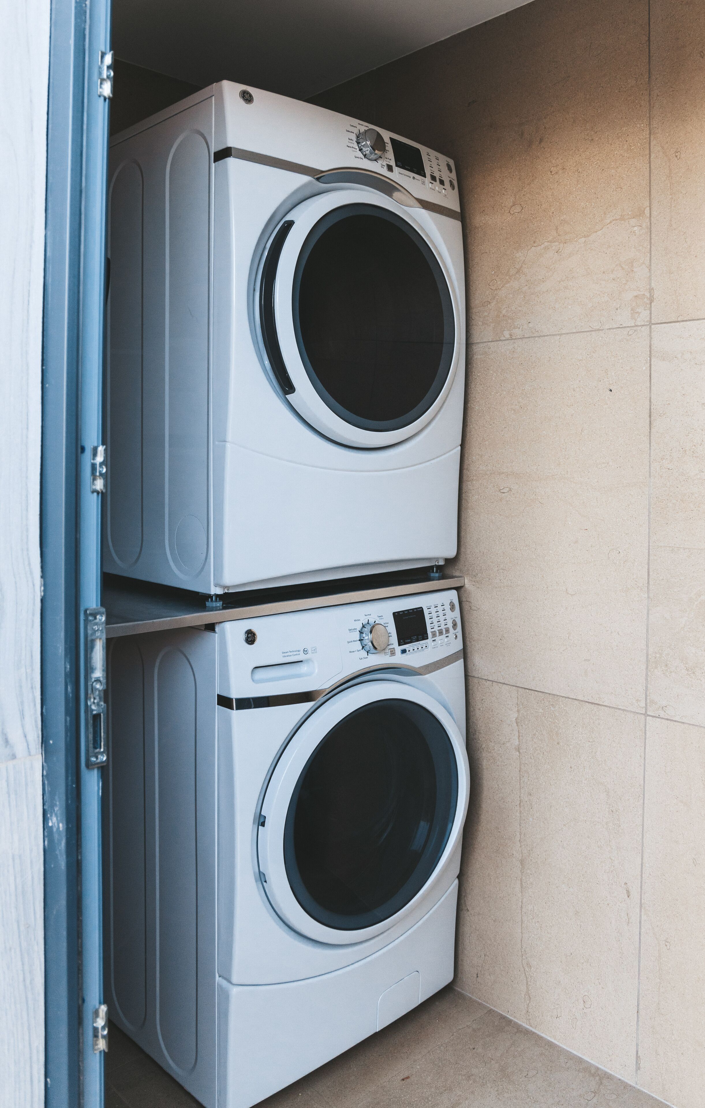 Twee boven elkaar geplaatste wasmachines met voorlader in een hoek, met betegelde wanden.