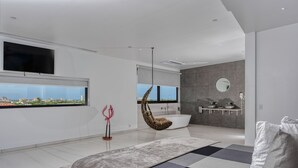 A modern bedroom with a large bed, a hanging chair, a bathtub, and a view of the city. - Gray Door Apartments - Adults Only (Noord)