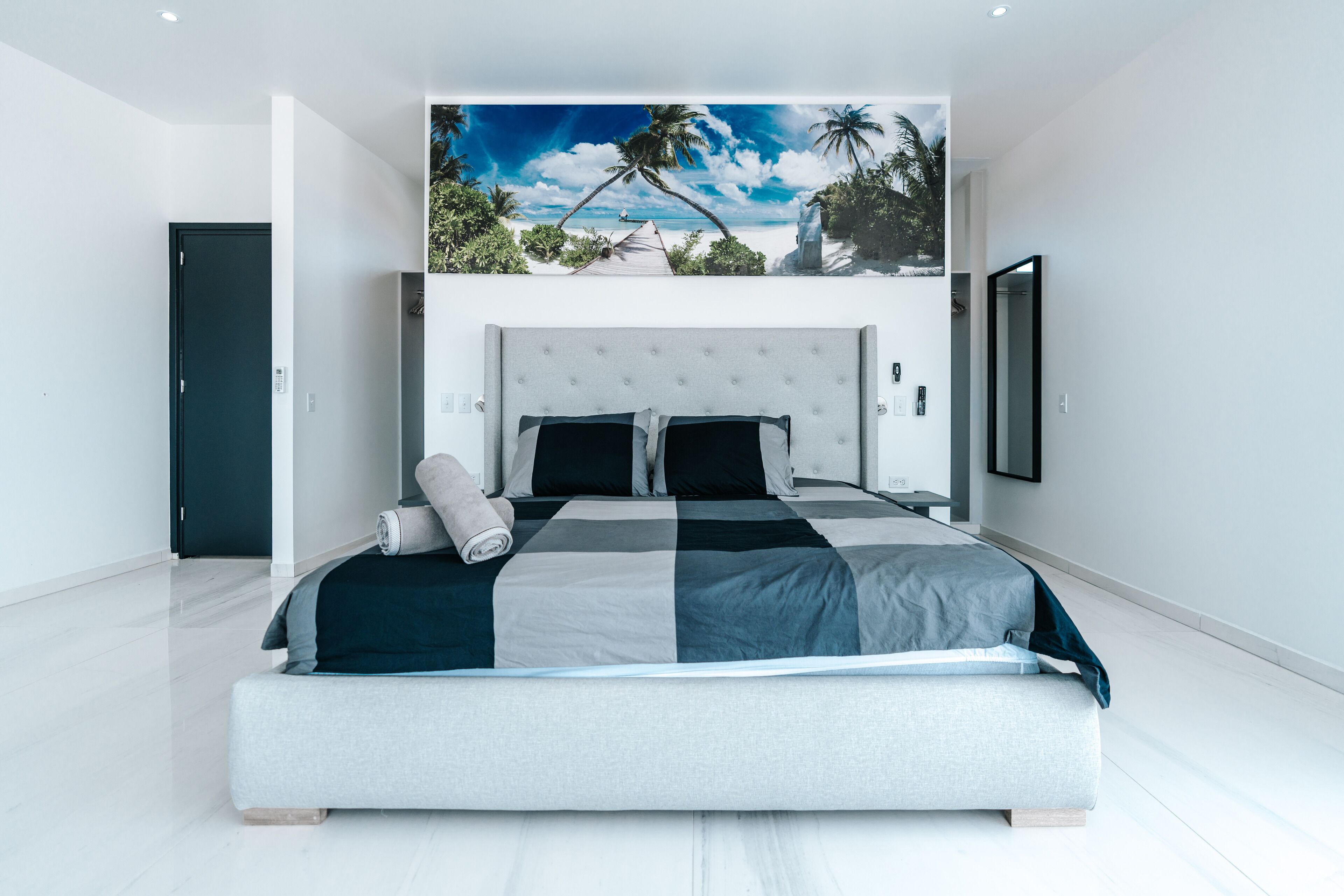 Een moderne slaapkamer met een groot bed, een hoofdeinde met uitzicht op een strand, en een deur aan de linkerkant.