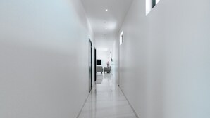 A modern, well-lit hallway with a glossy floor, leading to a seating area with a chair and a table. - Gray Door Apartments - Adults Only (Noord)