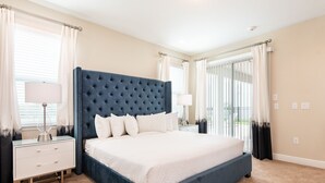 A bedroom with a large bed, a nightstand, a lamp, and a window with curtains. - Vivid Home near Disney: Theater, Themed Room & Waterpark - 7662FF (Reunion)