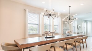 A spacious dining area with a long wooden table, multiple chairs, and a modern chandelier.