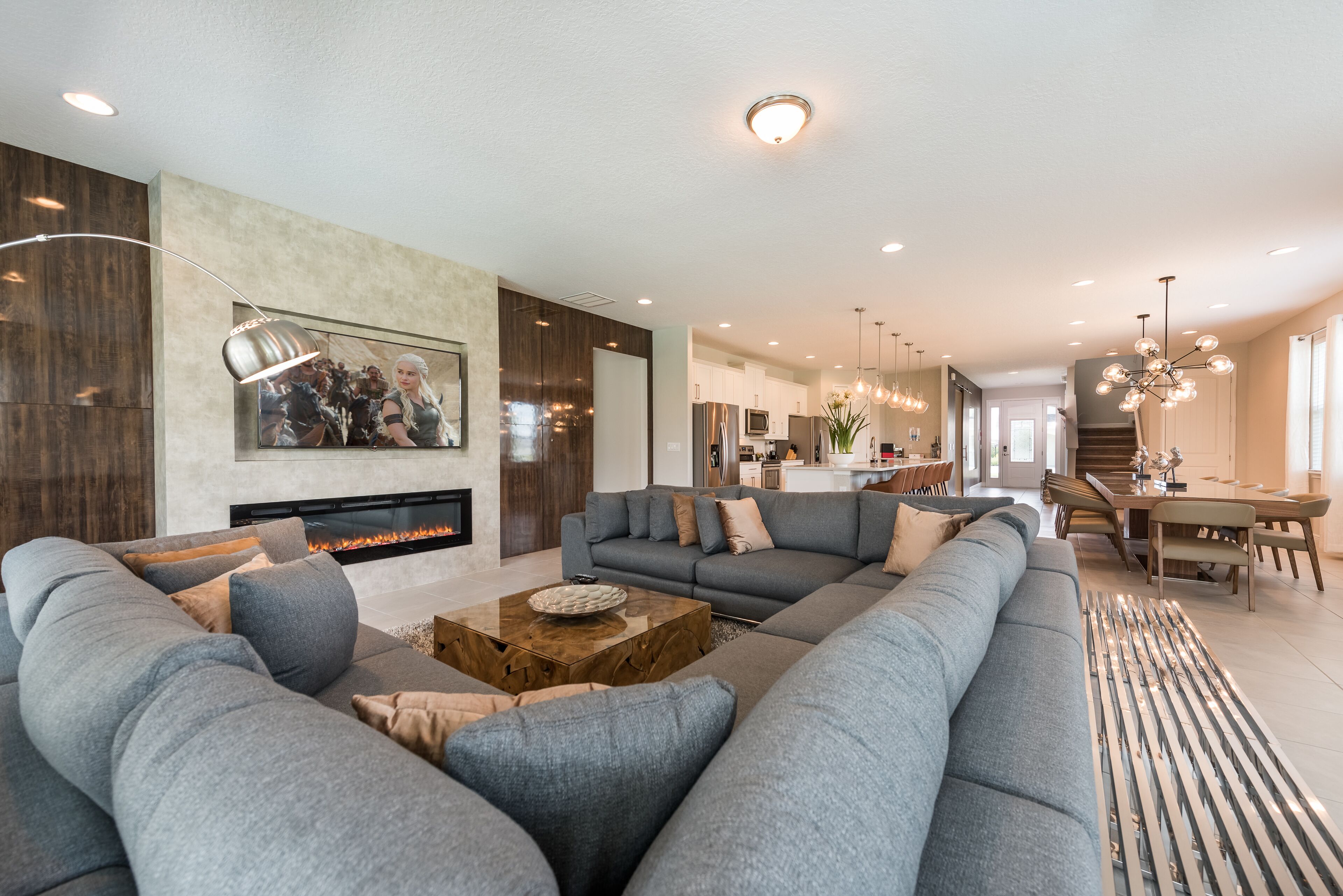A modern living room with a large sectional sofa, a fireplace, and a dining area with a chandelier.