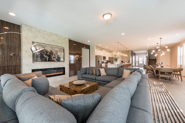 A modern living room with a large sectional sofa, a fireplace, and a dining area with a chandelier.