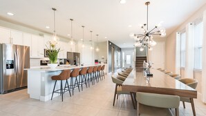 A modern kitchen with a central island, bar stools, and a dining table.
