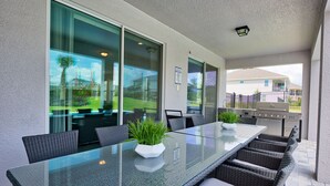 An outdoor patio with a glass-top table, wicker chairs, and a grill.