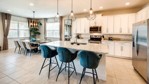 A modern kitchen with a central island, bar stools, white cabinets, stainless steel appliances, and pendant lighting.