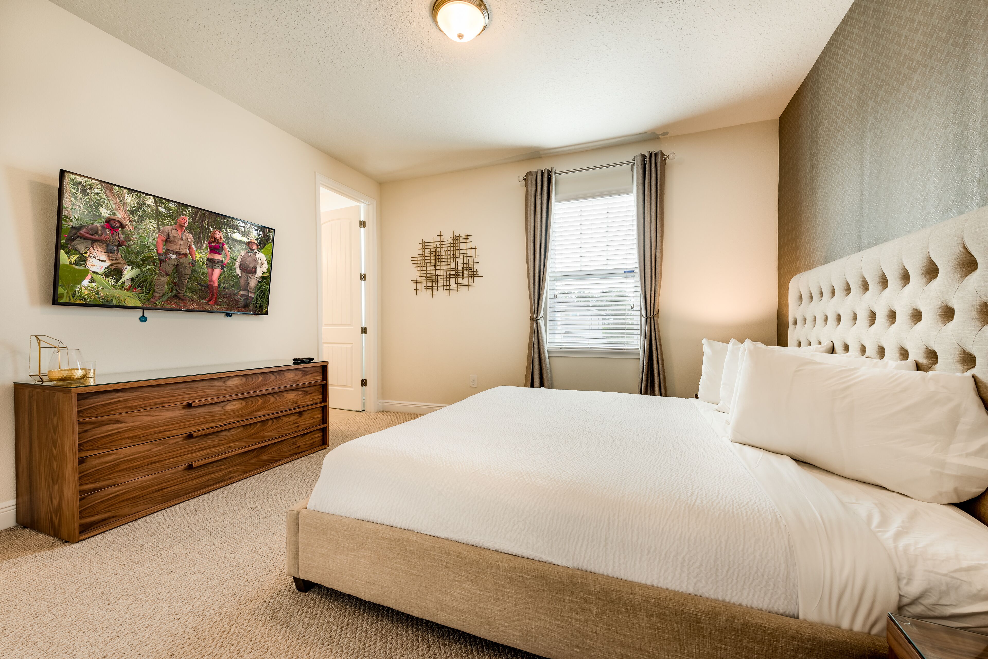 A bedroom with a large bed, a wooden dresser, a flat-screen TV, and a decorative wall piece.