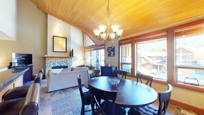 Amplia sala de estar con chimenea de piedra, una mesa de comedor con sillas, un sofá y un televisor.