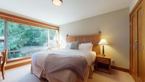 Un dormitorio con una cama grande, una mesita de noche, una lámpara, un armario y una ventana con vistas al verdor.