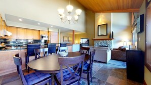 Una cocina moderna con armarios de madera, un comedor con mesa y sillas redondas, una chimenea de piedra y una sala de estar con sofá y televisión.