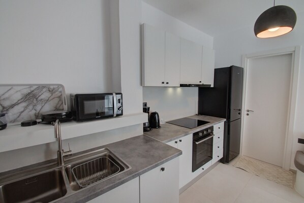 A modern kitchen with white cabinets, a black refrigerator, a microwave, and a sink.