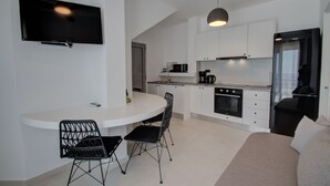 Eine moderne Küche mit weißen Schränken, einem schwarzen Kühlschrank und einem eingebauten Backofen. Es gibt einen Essbereich mit einem weißen Tisch und schwarzen Stühlen.