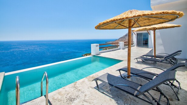 Ein Poolbereich mit freiem Blick auf den Ozean, Liegestühle und ein Strohdachschirm.