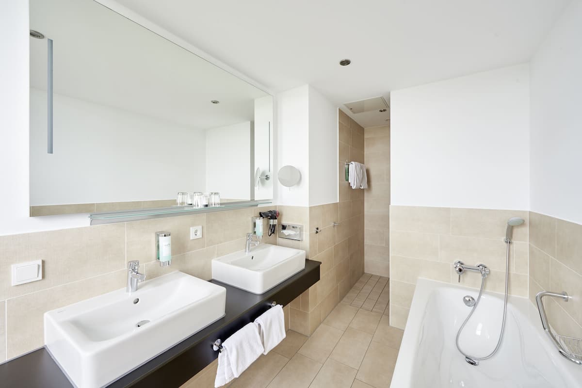 A modern bathroom with two sinks, a large mirror, a bathtub, and a shower.