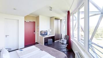 A hotel room with a bed, desk, chair, and large windows.