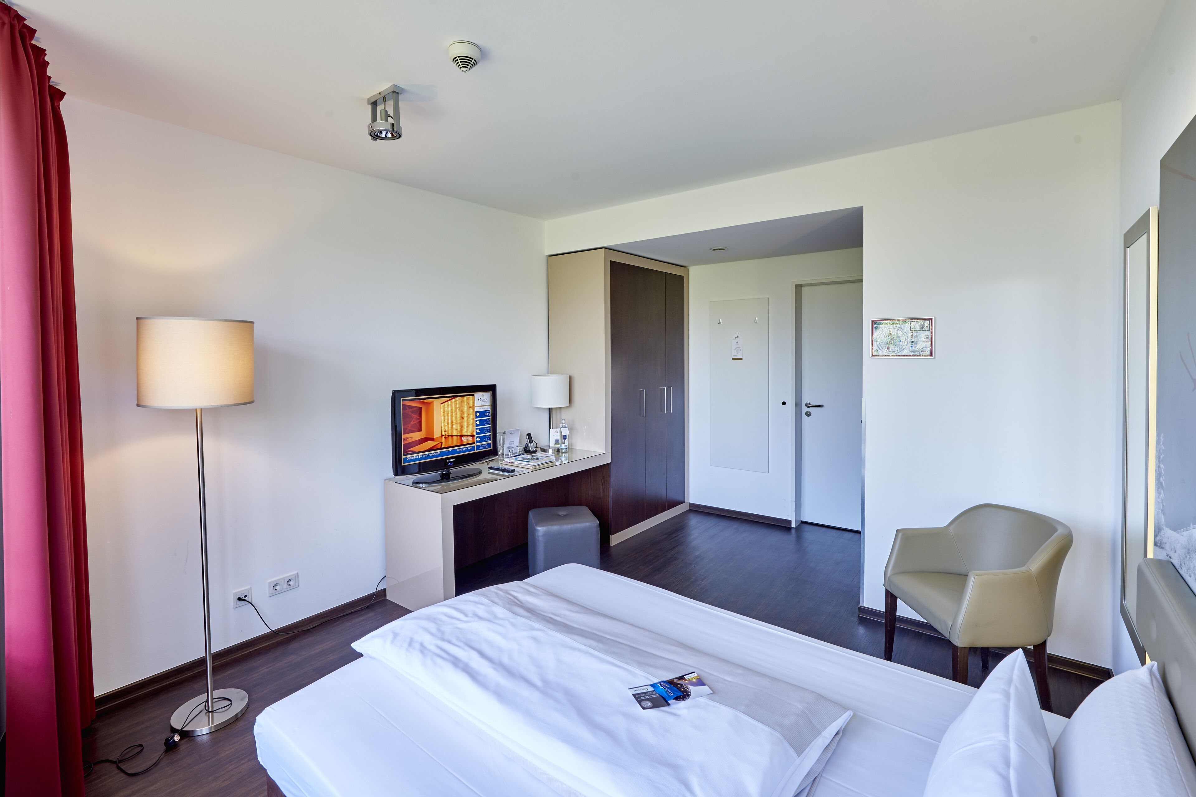 Une chambre d’hôtel comprenant un lit, un bureau, une chaise, une télévision et une porte donnant sur une autre pièce.