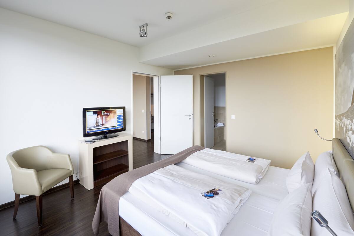 A hotel room with a bed, a TV on a stand, a chair, and a wardrobe.